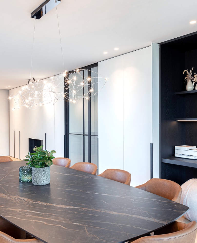 Totaalinrichting in Zarren (regio Diksmuide) met zwarte maatwerknis, designverlichting en grote zwarte keramische eettafel met leren stoelen.