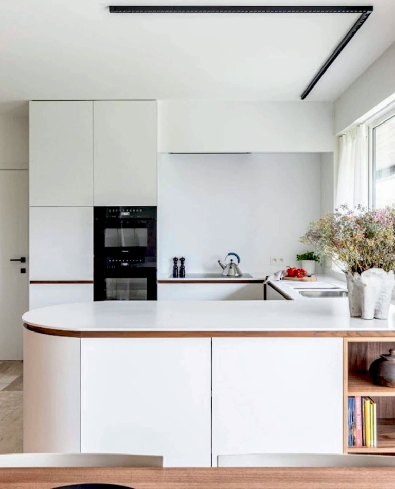 Lichte, moderne maatkeuken in Roeselare, Diksmuide, West-Vlaanderen met witte kasten, notenhouten accenten en bloemstuk op het werkblad.