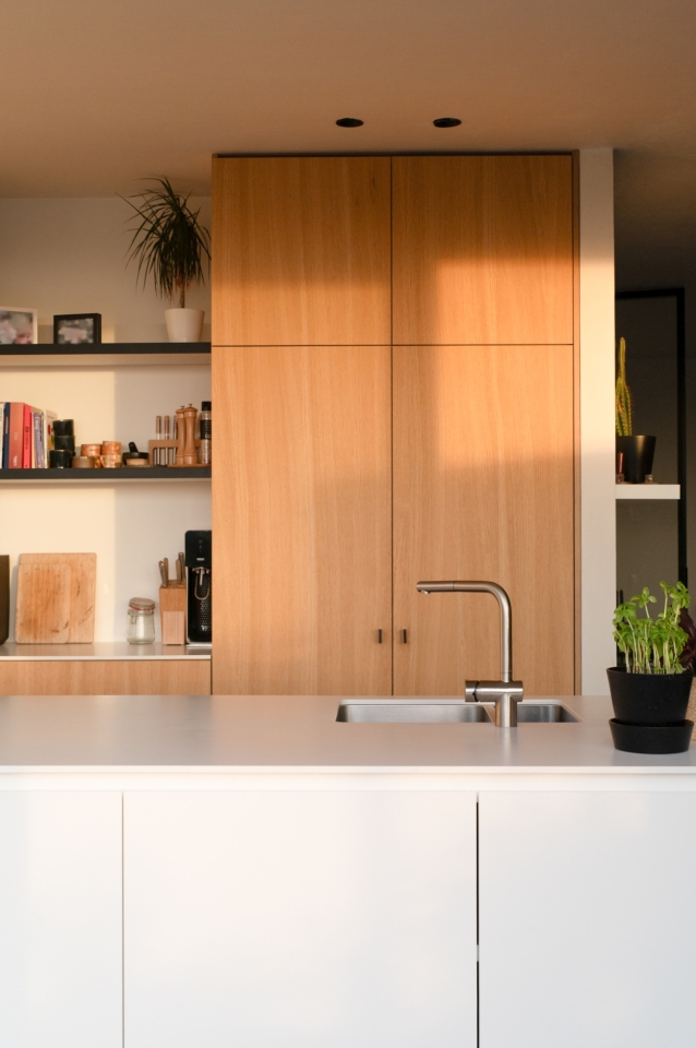 Moderne keuken op maat met houten kastenwand, strakke witte eilandkast en geïntegreerde inox kraan.