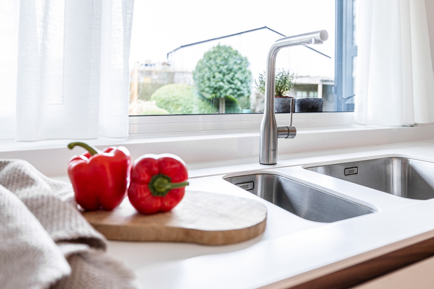 Lichte moderne keuken in West-Vlaanderen met Corian werkblad, dubbele inox spoelbak en roestvrijstalen designkraan – strak en minimalistisch keukenontwerp door Abstrakt Interieur.