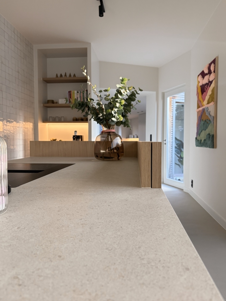 Detail van het keukeneiland met natuursteen werkblad en eiken maatwerk, uitgevoerd in een rustig interieur in Roeselare, West-Vlaanderen