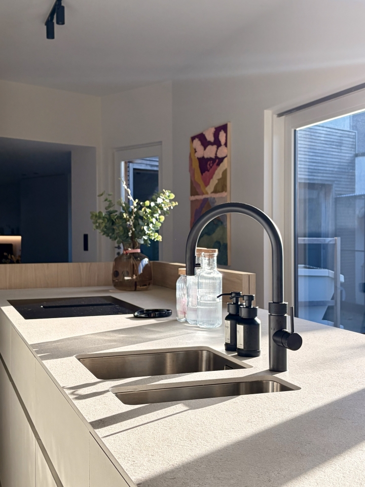 Detail van het keukeneiland met geïntegreerde spoelbak en zwarte kraan, uitgevoerd in een rustig maatwerkinterieur in Roeselare, West-Vlaanderen